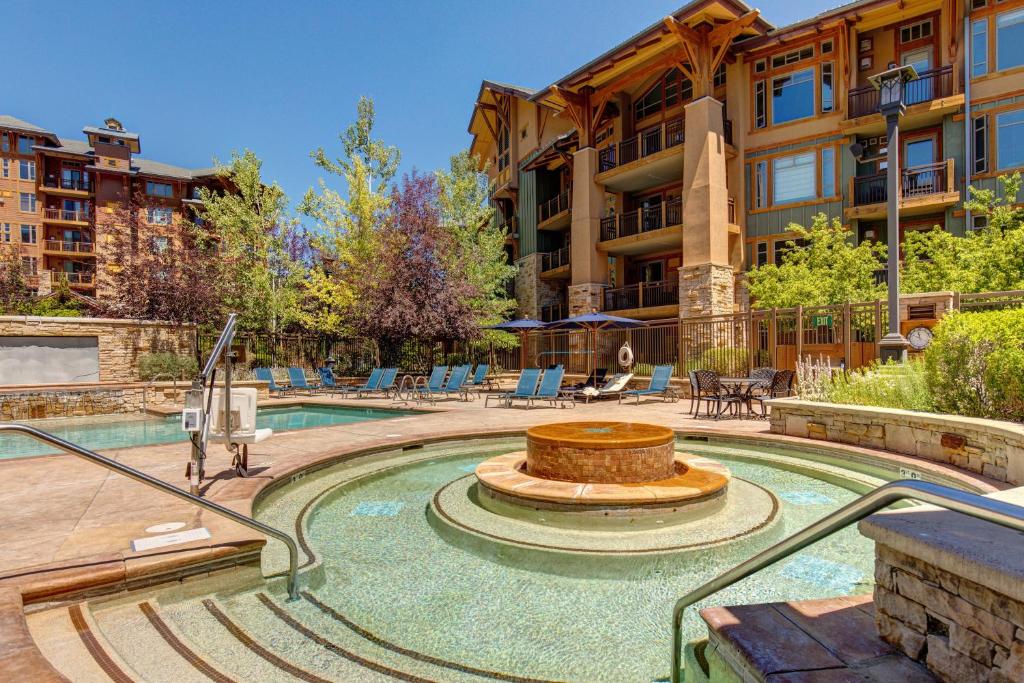 A resort-style outdoor pool area with lounge chairs, trees, and a hot tub in front of a building.