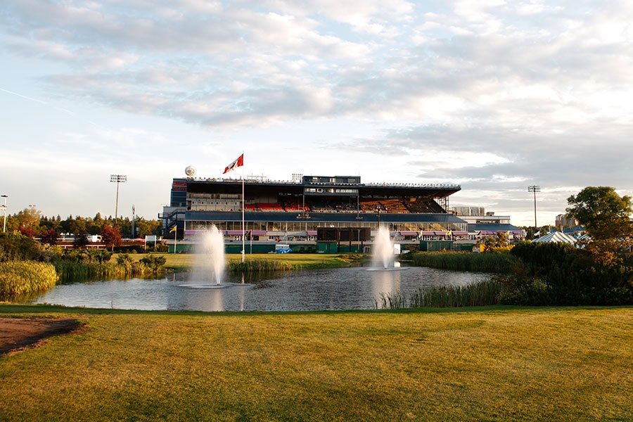 The spacious outdoor view of Northlands Park Racetrack and Casino in Alberta, featuring a serene pond with fountains, green surroundings, and the grandstand under a partly cloudy sky.