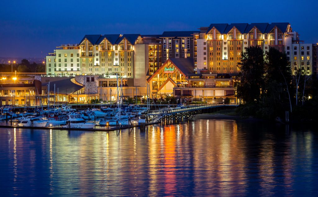 "River Rock Casino Resort, BC: A luxurious waterfront resort glowing at night, with reflections on the marina and docked boats adding charm." 