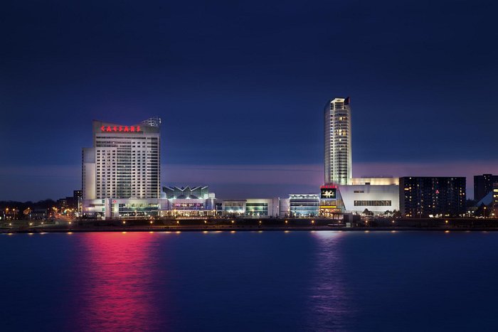 Caesars Windsor in Ontario illuminated at night, reflecting vibrant lights over the Detroit River.
