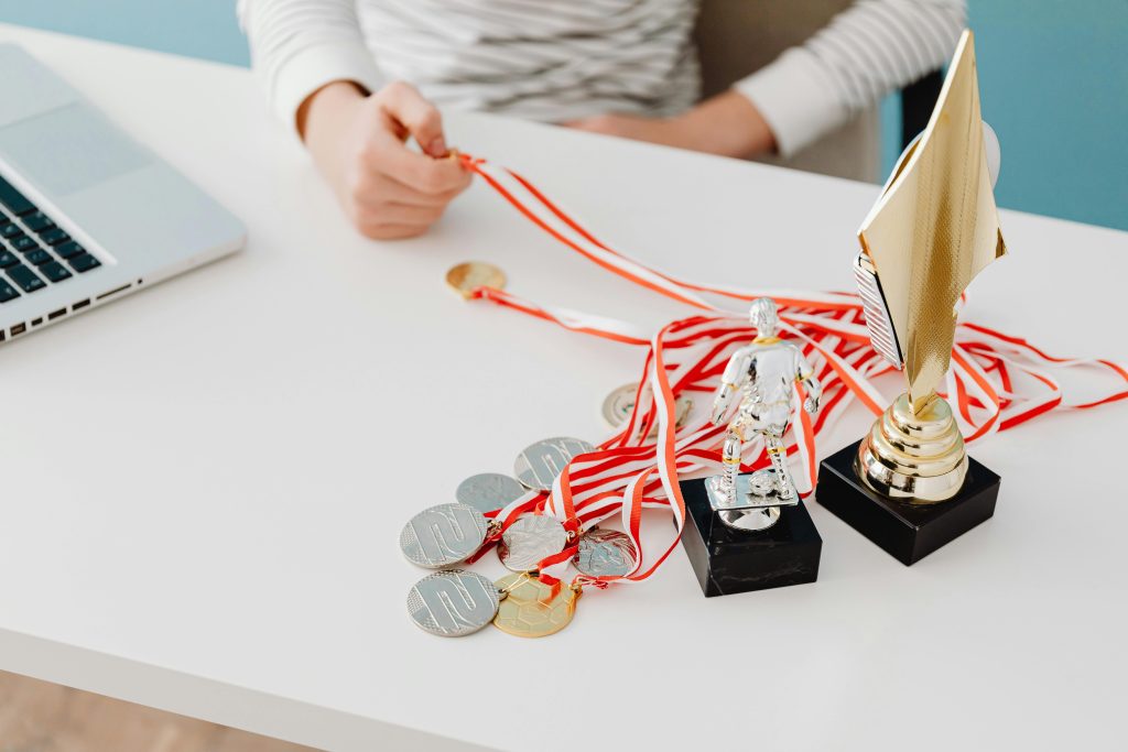 Awards & Recognition :- "Medals and trophies on a desk with a laptop nearby."